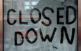 Hand painted “Closed Down” sign on a storefront window with reflections of the street outside