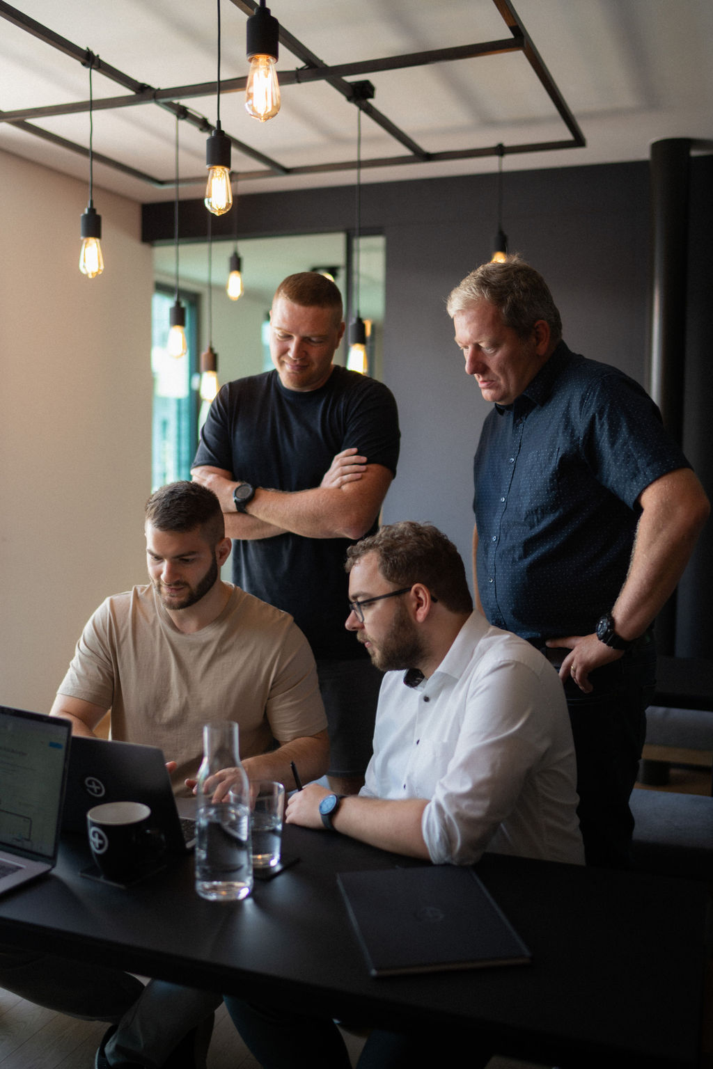 Troi team collaborating around a laptop during a project planning session, reviewing schedules, budgets and PSA workflows in a modern professional services office environment