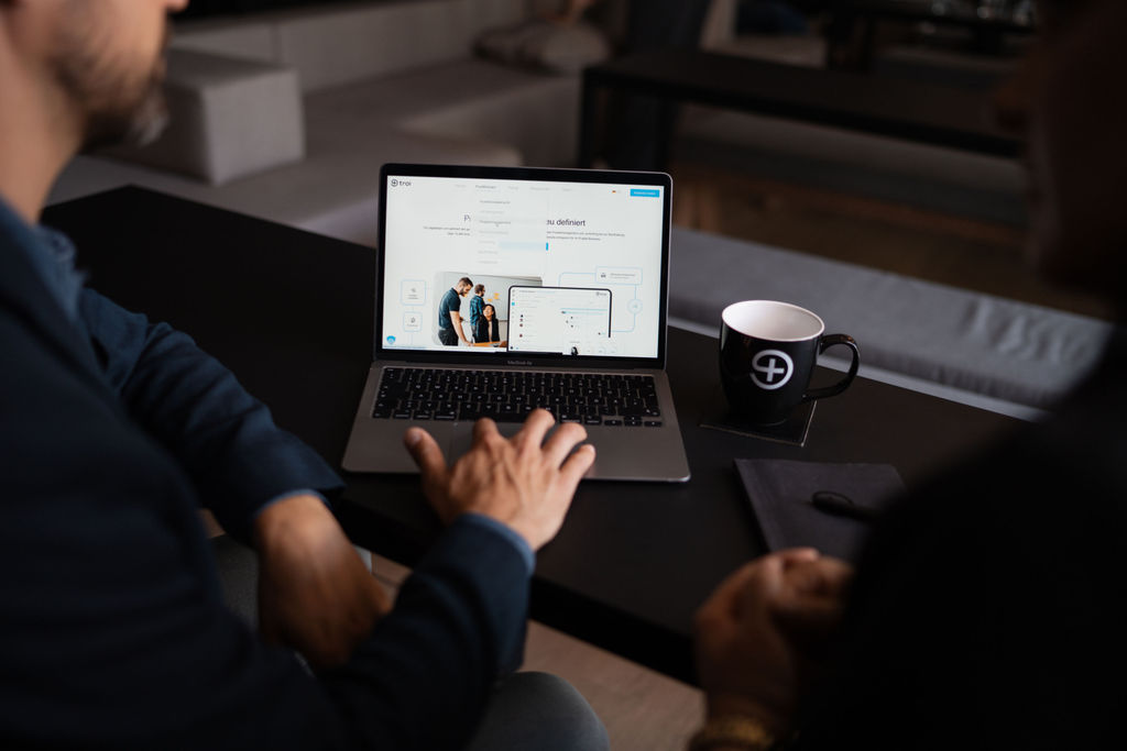 Troi web interface displayed on a laptop during a product demo with a branded coffee mug on the table in a modern office setting