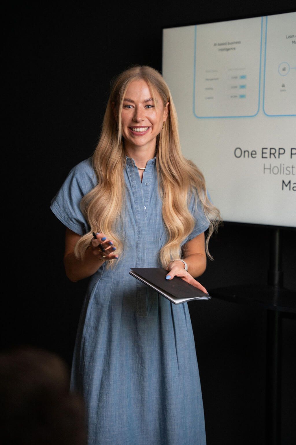 Troi team member presenting software insights with a tablet in front of a screen showing ERP and AI powered dashboard elements during a product demonstration