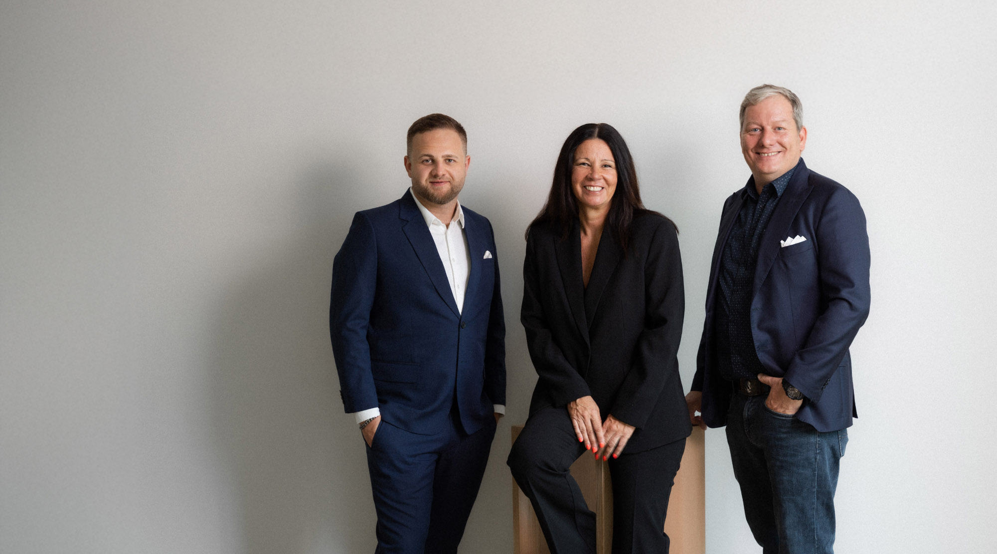 Three business executives standing together against a light studio wall, wearing formal business clothing, presenting the leadership team of the Troi software company in a professional portrait